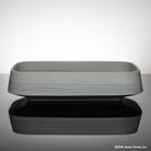 Rectangular gray vessel sink carved from grigio sandstone on a reflective surface with a light gray background