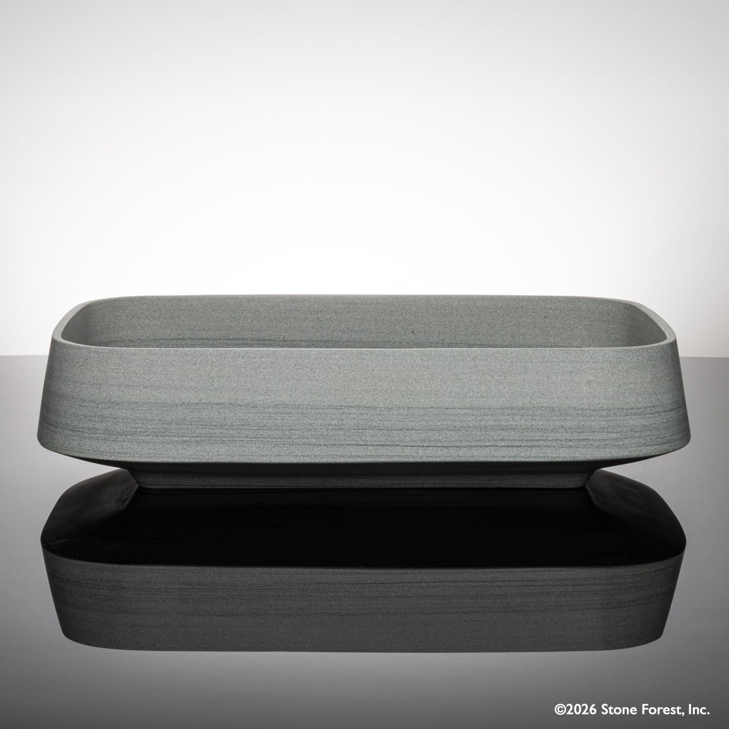 Rectangular gray vessel sink carved from grigio sandstone on a reflective surface with a light gray background