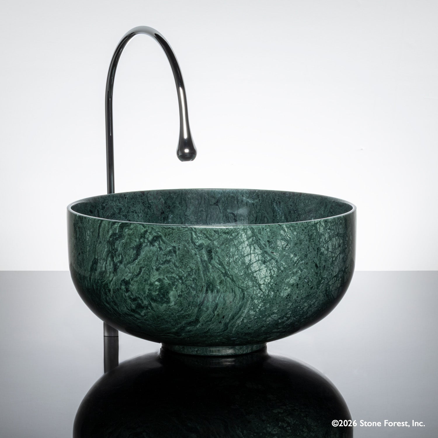 Green marble vessel sink with a faucet on a reflective surface