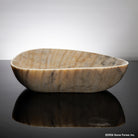 Honey onyx stone vessel sink on a reflective black surface with a dark gray background