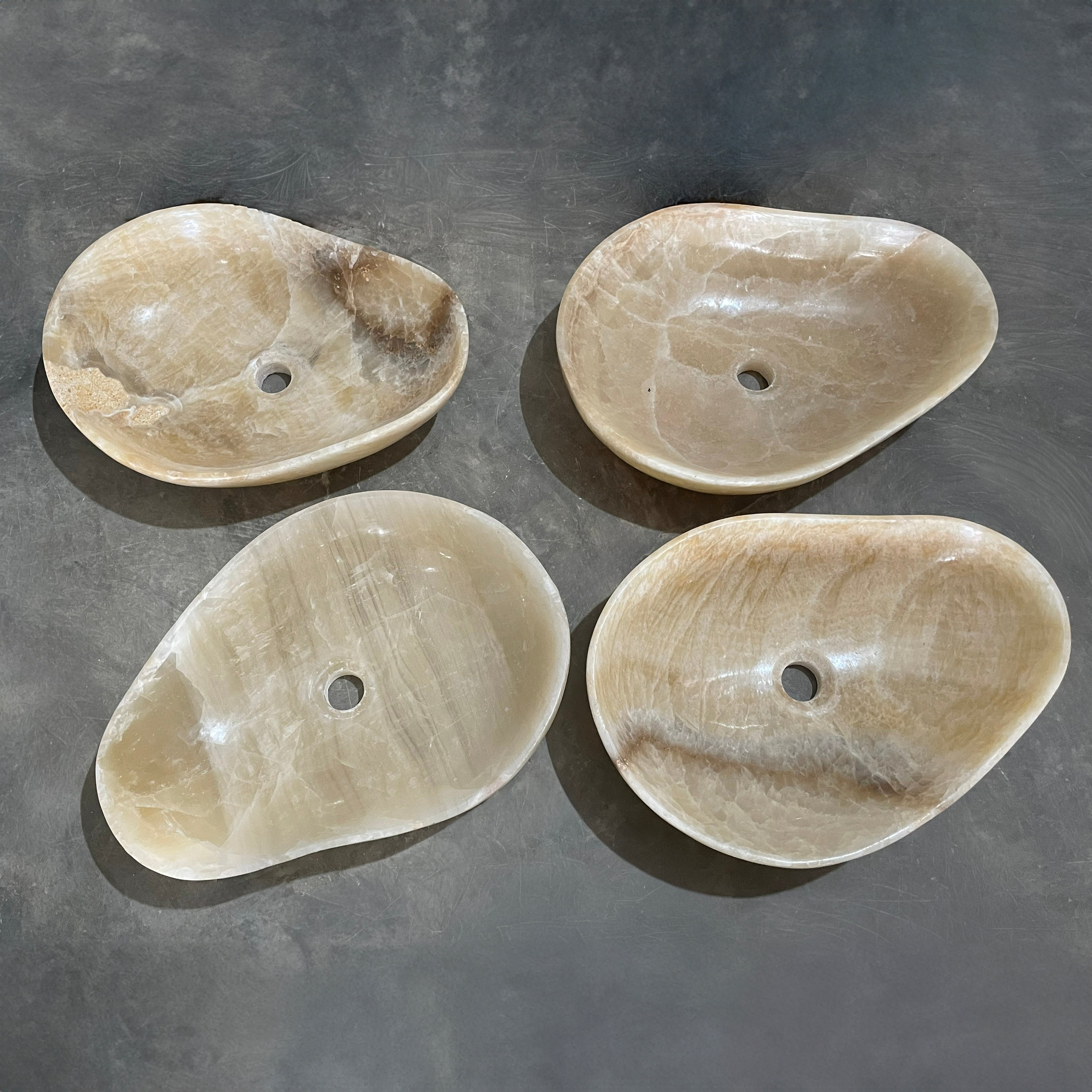 Four honey onyx stone sinks on a gray surface