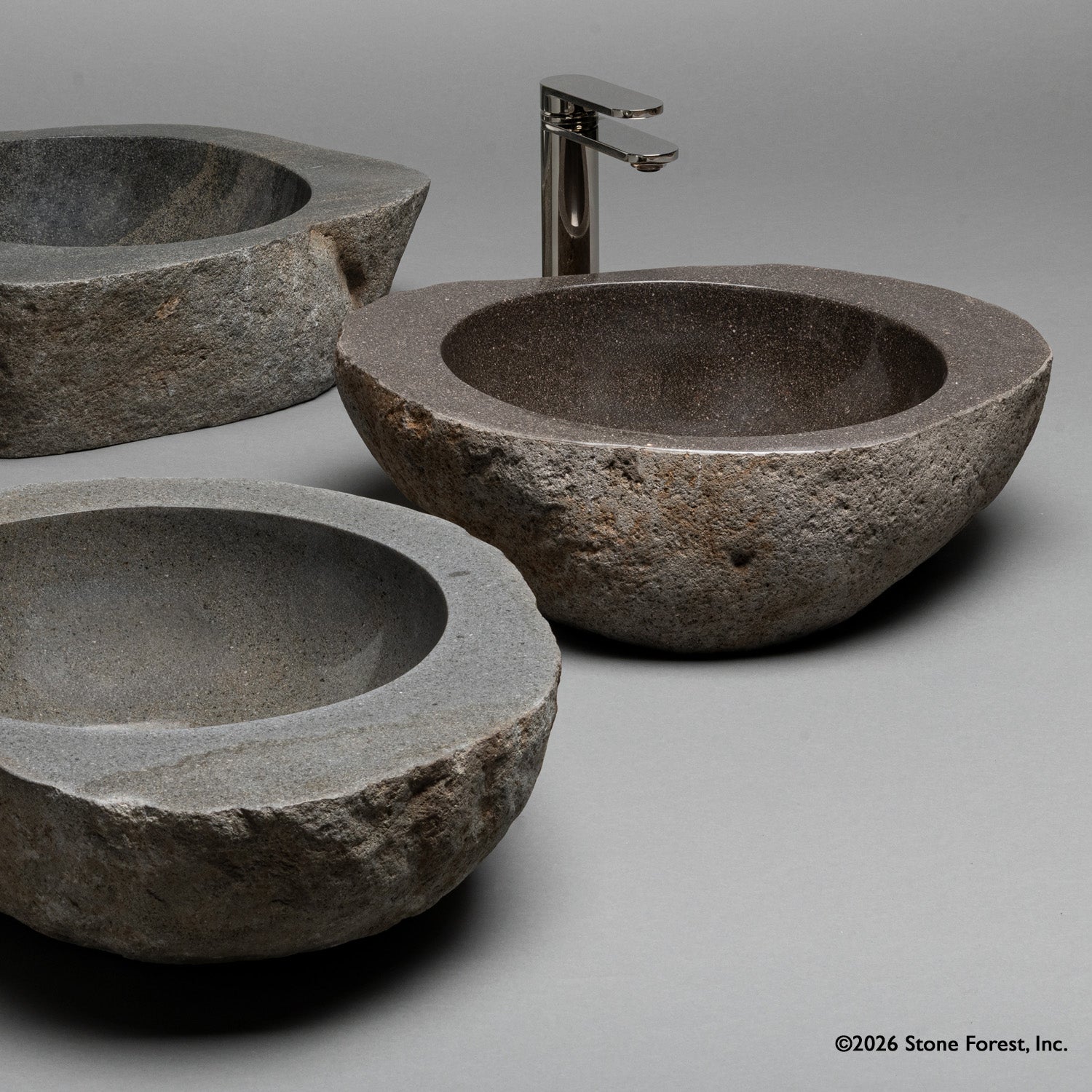 Three natural stone sinks with a faucet on a gray background