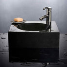 A black granite vessel sink with an offset circular basin, mounted on a dark countertop