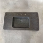 An antique gray limestone sink with a rectangular shape, featuring a central integral sink and sitting on a plain surface.