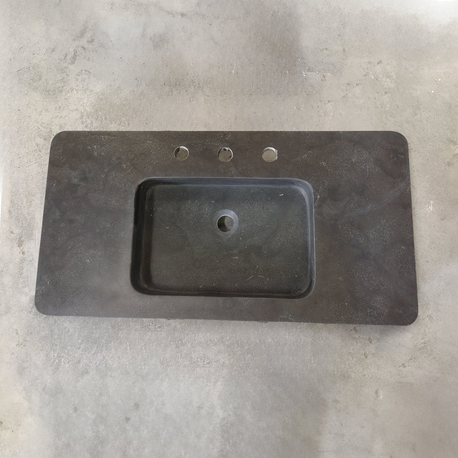 An antique gray limestone sink with a rectangular shape, featuring a central integral sink and sitting on a plain surface.