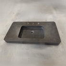An antique gray limestone sink with a rectangular shape, featuring a central integral sink and sitting on a plain surface.