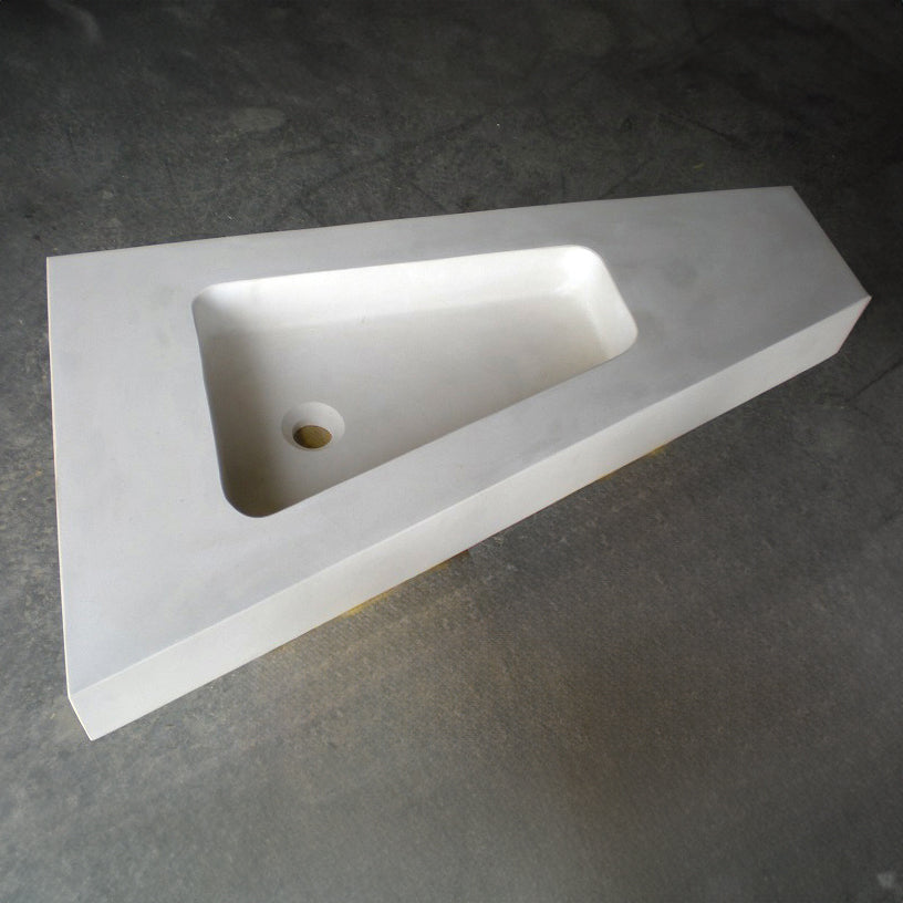 A trapezoid shaped sink made of desert creme limestone, placed on a grey surface.