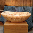 An oval-shaped honey onyx sink is placed on a wooden stand.