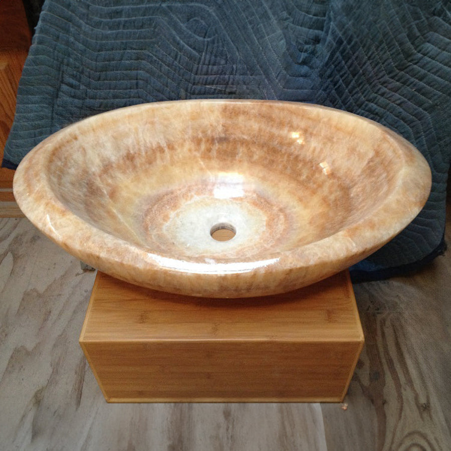 An oval-shaped honey onyx sink is placed on a wooden stand.