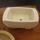 A beige, rectangular vessel sink made of Papiro cream marble, placed on a wooden surface.