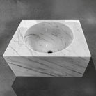 A custom rectangle sink in Carrara marble, with a white and gray color pattern, placed on a dark surface.
