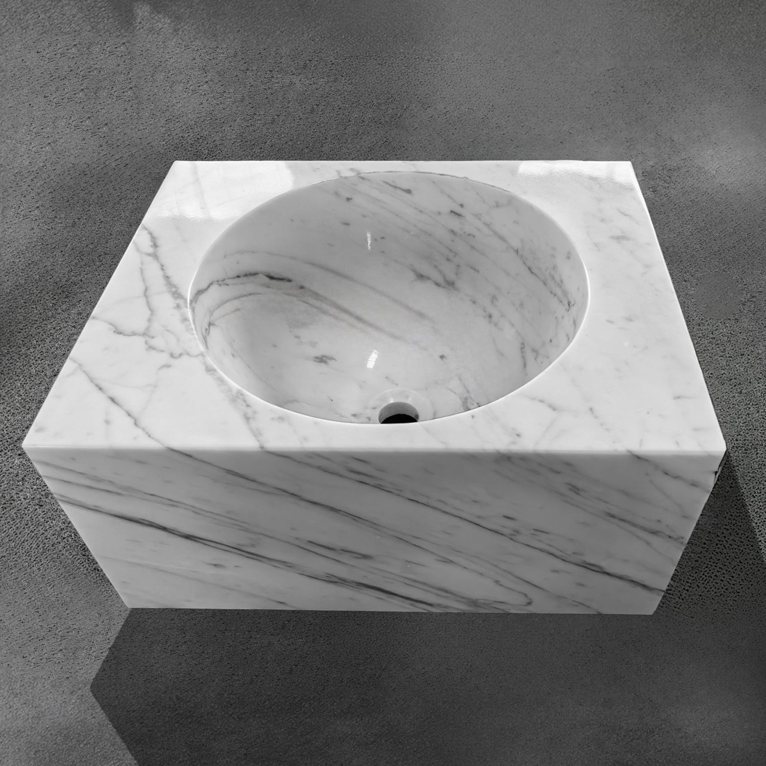 A custom rectangle sink in Carrara marble, with a white and gray color pattern, placed on a dark surface.