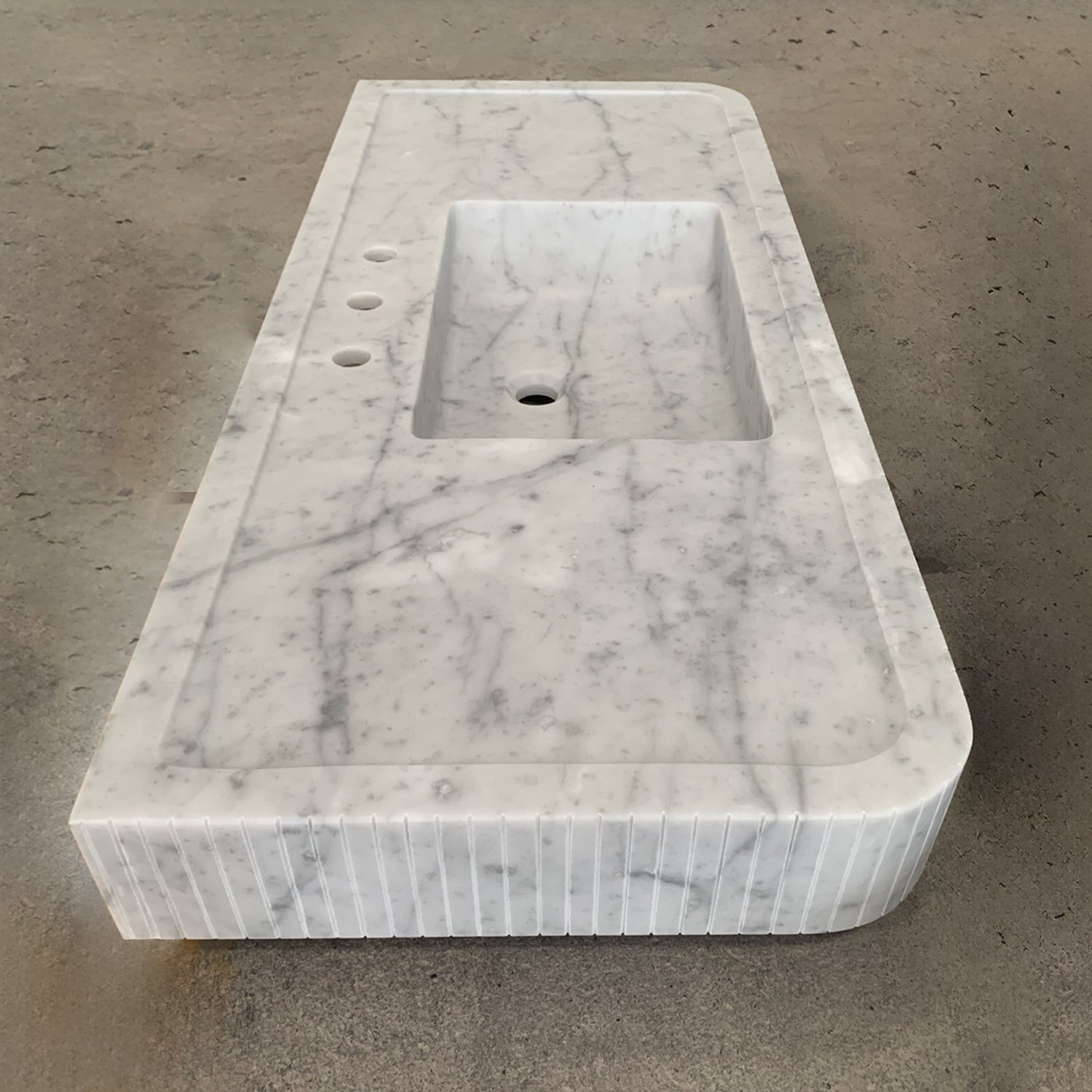 A white marble vanity with a fluted front, featuring an integral sink.