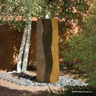 A large basalt column fountain with a polished black and gold stone surface, displayed outoors