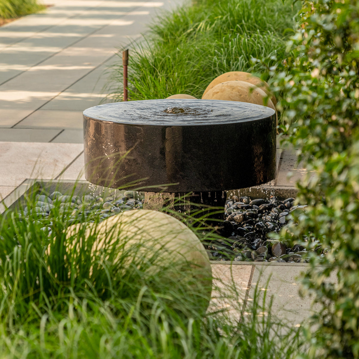 Polished black granite Millstone Fountain installed in garden, surrounded by granite spheres