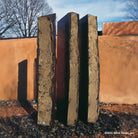 A vertical, columnar basalt fountain installed on a bed of pebbles, with natural weathered exterior and mirror polish surfaces.
