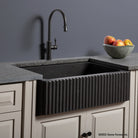 A black fluted front farmhouse sink installed in a kitchen counter with a modern faucet above it. The sink is carved from noce basalt and has a ribbed front design.