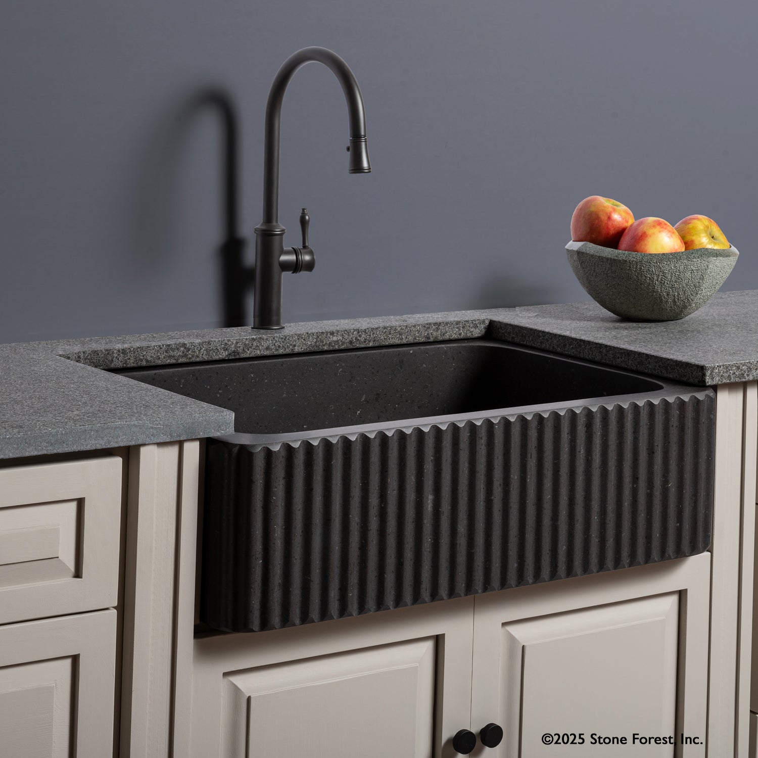 A black fluted front farmhouse sink installed in a kitchen counter with a modern faucet above it. The sink is carved from noce basalt and has a ribbed front design.