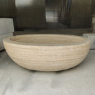 An oval-shaped, beige travertine marble tub.
