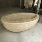 An oval-shaped, beige travertine marble tub.