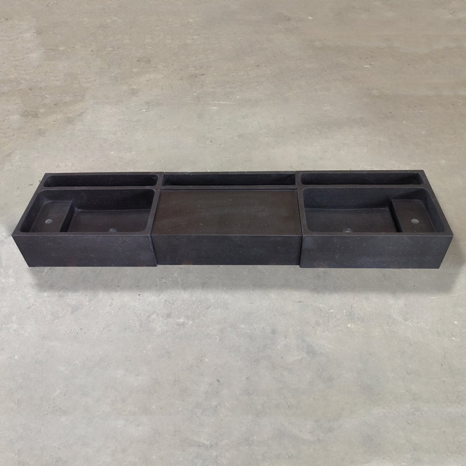 A three-piece black vanity sink made of basalt, placed on a concrete surface.