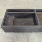 Detail of a three-piece black vanity sink made of basalt, placed on a concrete surface.