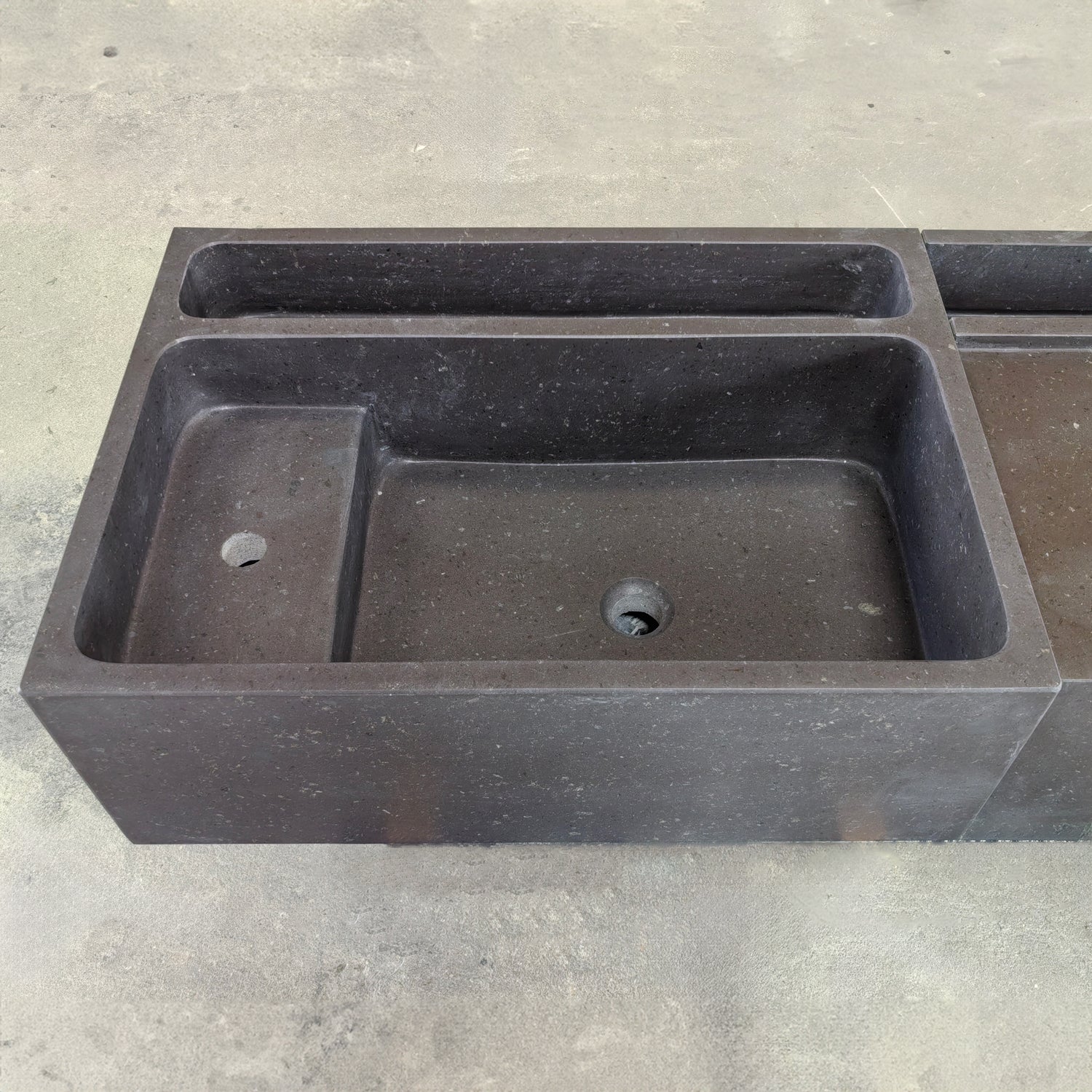 Detail of a three-piece black vanity sink made of basalt, placed on a concrete surface.