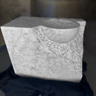 A Carrara marble vanity with a rough chisel design, displayed against a dark, textured background.