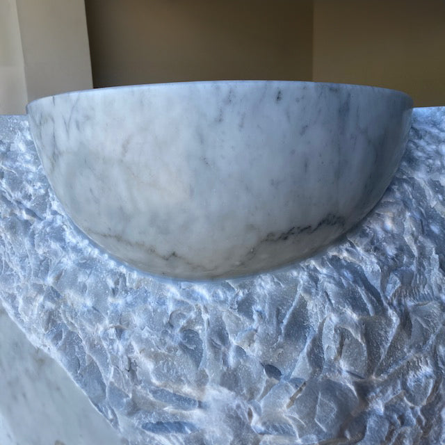 Detail of a Carrara marble vanity with a rough chisel design.