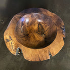 A hand-carved teak wood bowl with a smooth finish, showing natural wood grain, is displayed on a concrete surface 
