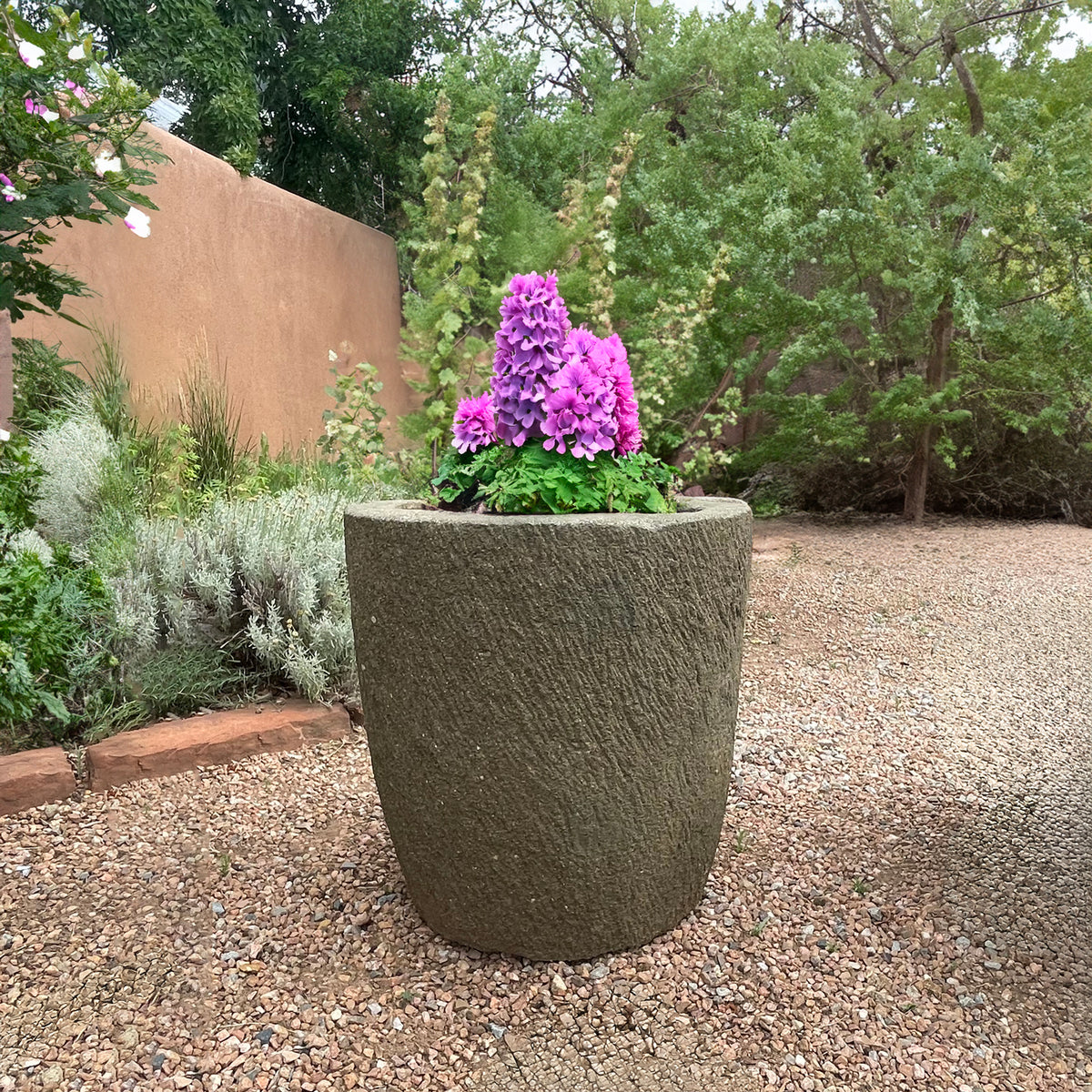 Decorative stone planter with purple flowers in a garden setting image 2 of 5