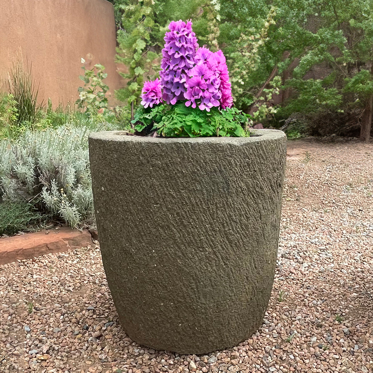 Large stone planter with purple flowers in a garden setting image 1 of 5