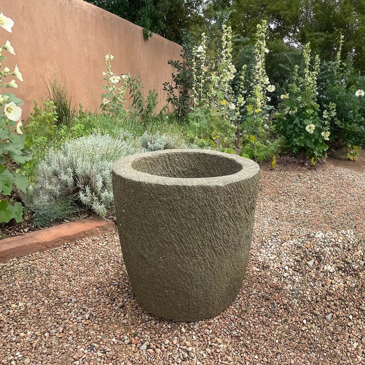 Textured stone planter in a garden setting with plants and a wall in the background image 3 of 5