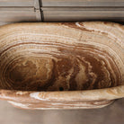 A large, oval-shaped, multi-color onyx planter placed on a concrete floor with wooden vertical elements in the background.