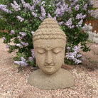 Stone Buddha head statue in a garden with purple flowers