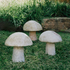 Three garden mushrooms carved from onyx, placed in a garden setting.