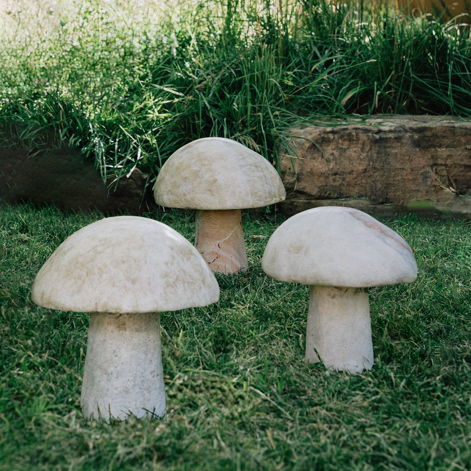 Three garden mushrooms carved from onyx, placed in a garden setting.