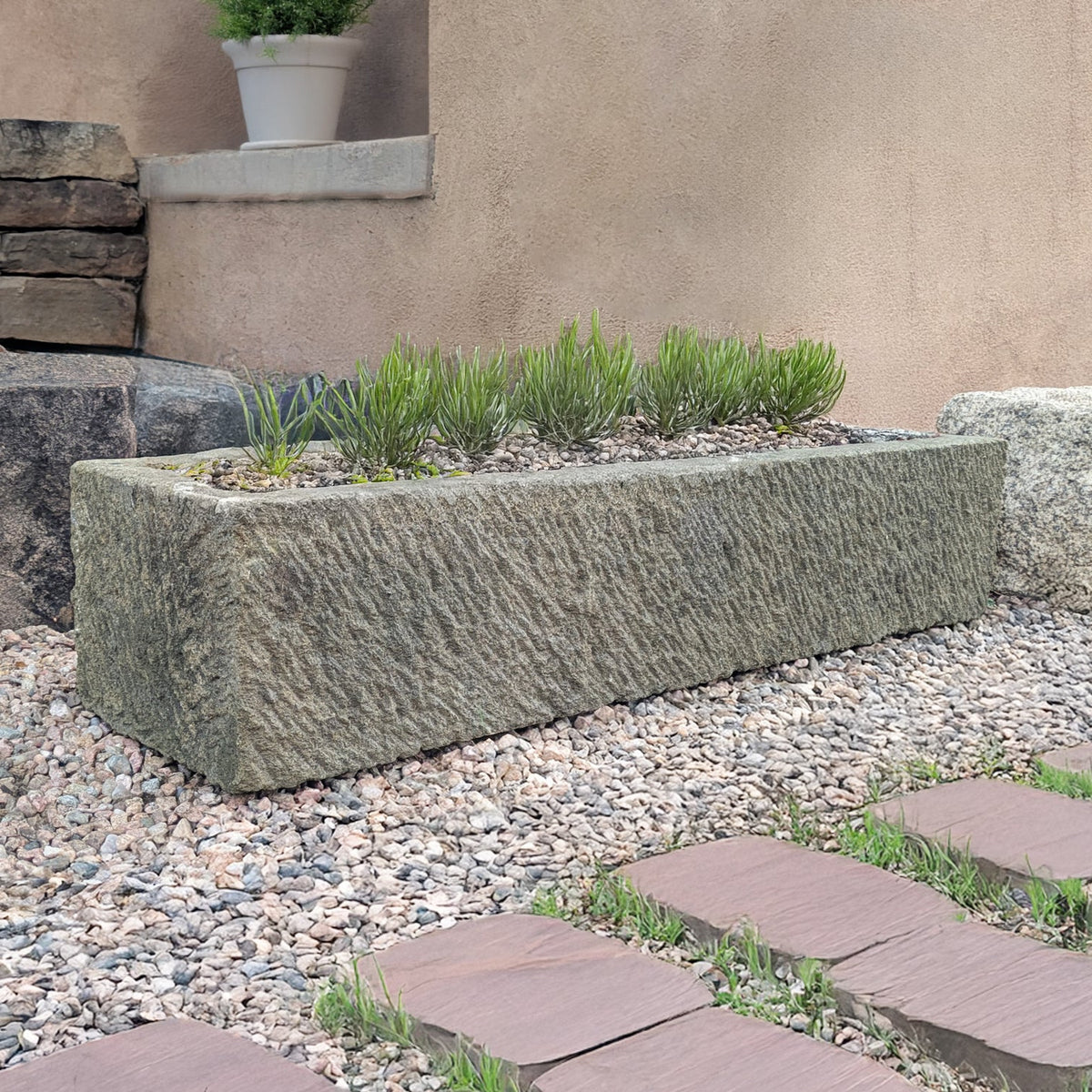 Decorative stone planter with plants against a beige wall. image 3 of 3