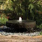 A round natural stone millstone fountain with water cascading over the edge.
