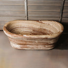 A large, oval-shaped, multi-color onyx planter placed on a concrete floor with wooden vertical elements in the background.
