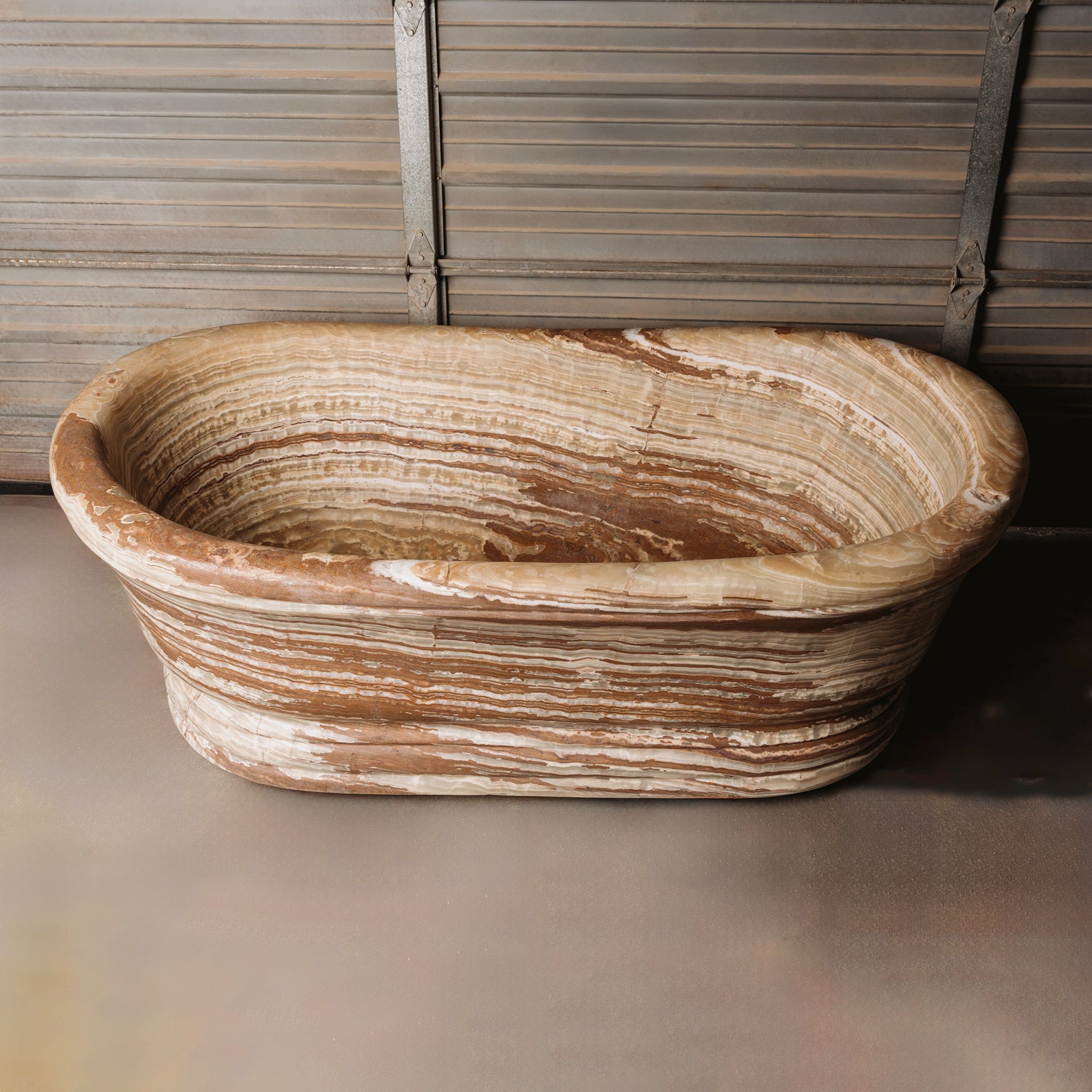 A large, oval-shaped, multi-color onyx planter placed on a concrete floor with wooden vertical elements in the background.