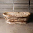 A large, oval-shaped, multi-color onyx planter placed on a concrete floor with wooden vertical elements in the background.