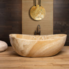 A honey onyx Bateau Bathtub placed on a wooden floor against a wooden wall, with a pendant light hanging above it.