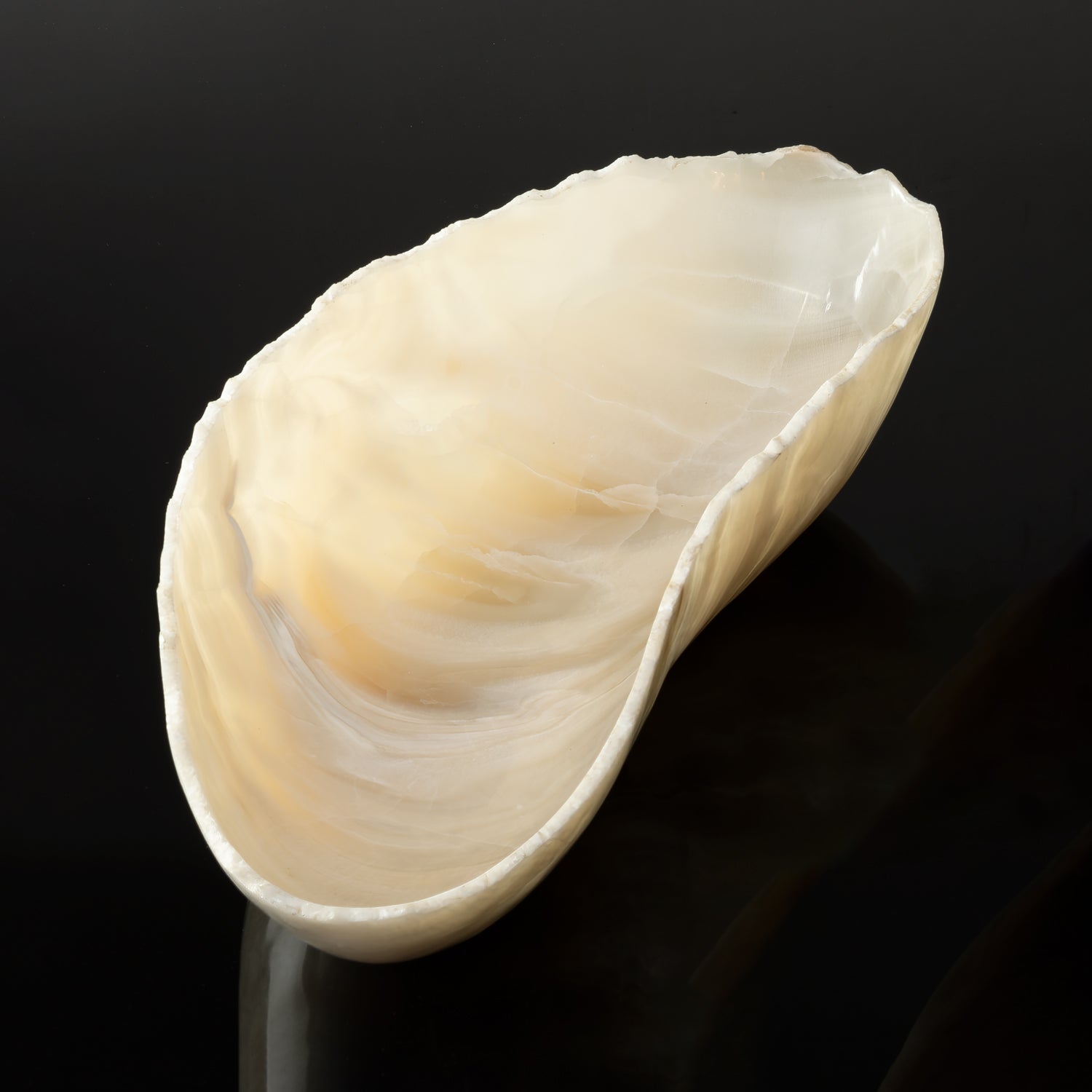 A free form onyx bowl with a smooth, curved shape against a dark background.