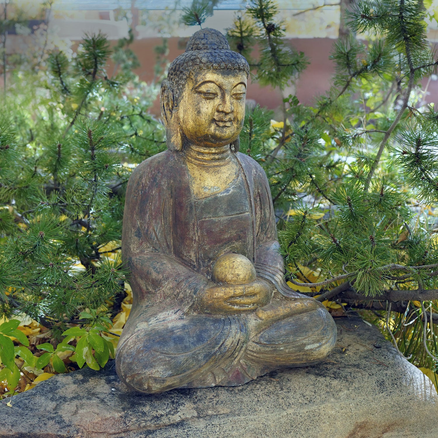 A hand-carved dark limestone Buddha statue with a painted finish, seated 