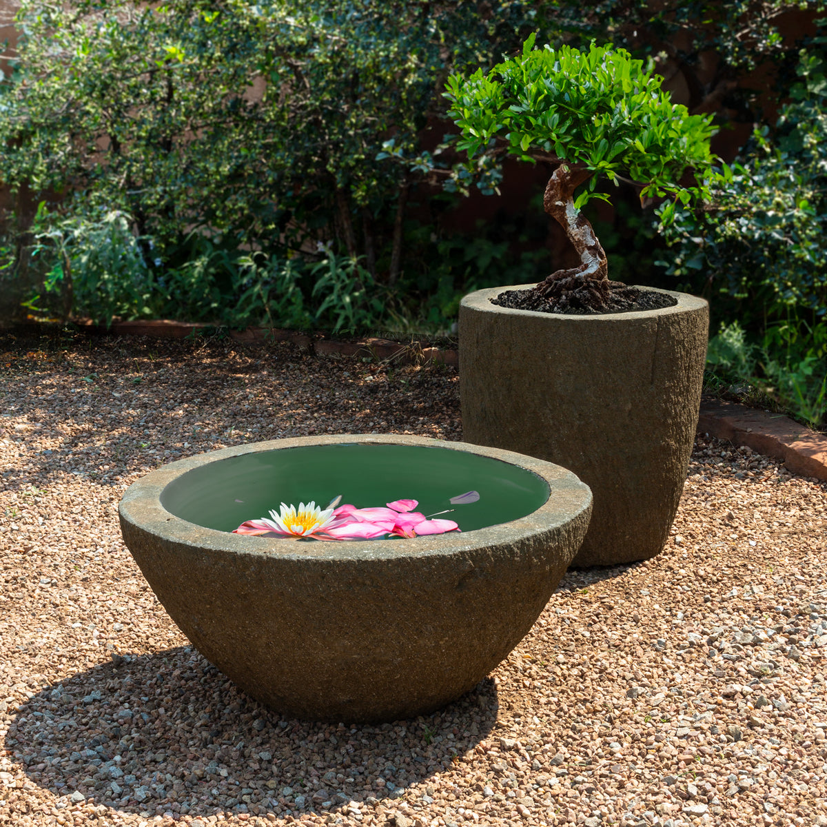 Two stone planters with a small pond and floating flowers in a garden setting. image 5 of 5