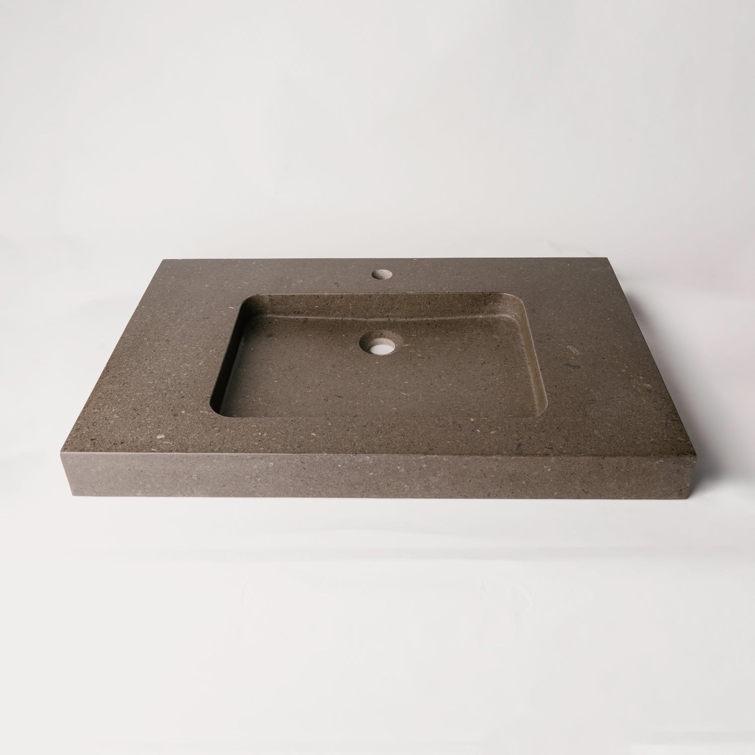 A contemporary bath vanity with an integral sink carved from a solid block of noce basalt. It has a center-hole faucet drilling.