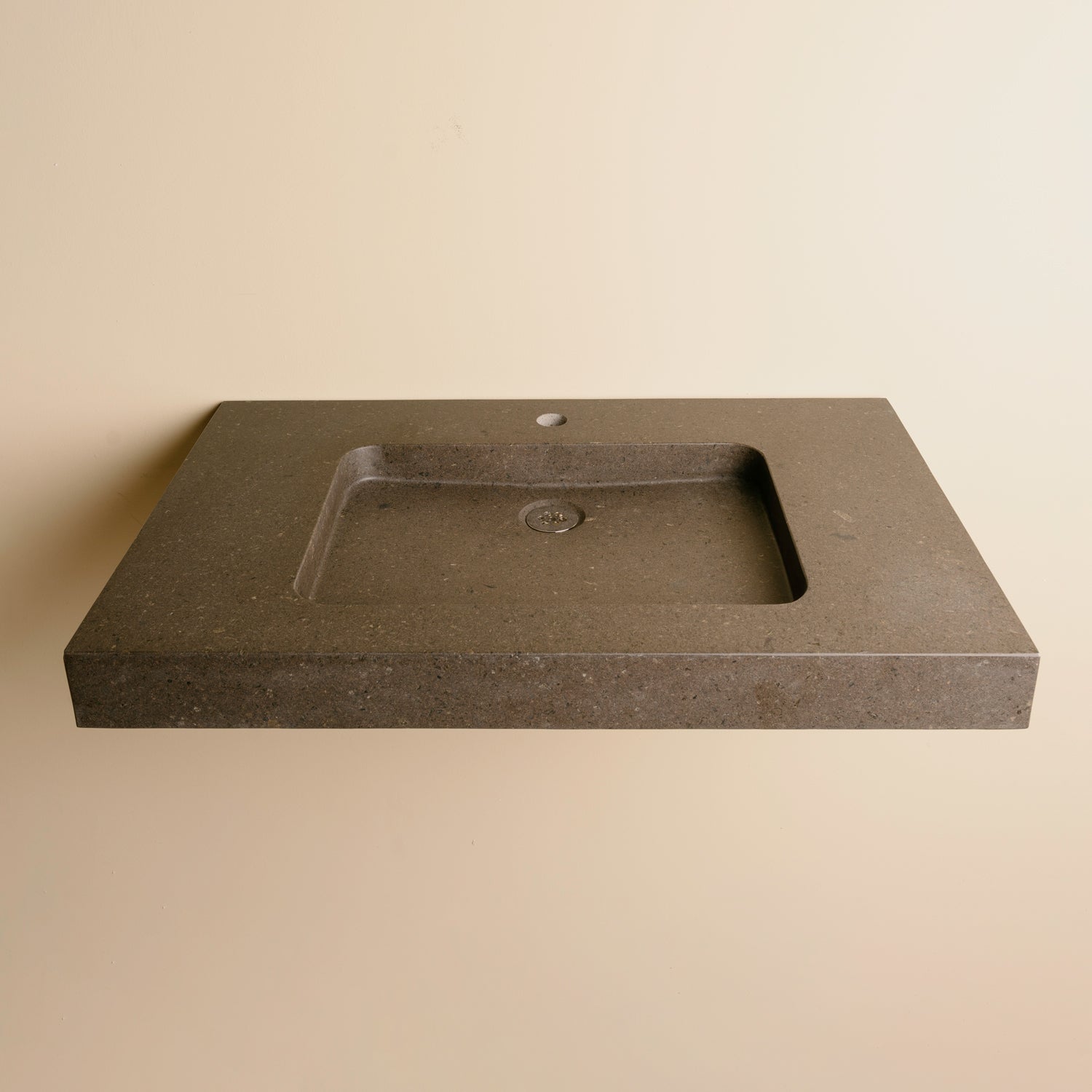 A contemporary bath vanity with an integral sink carved from a solid block of noce basalt. It has a center-hole faucet drilling.