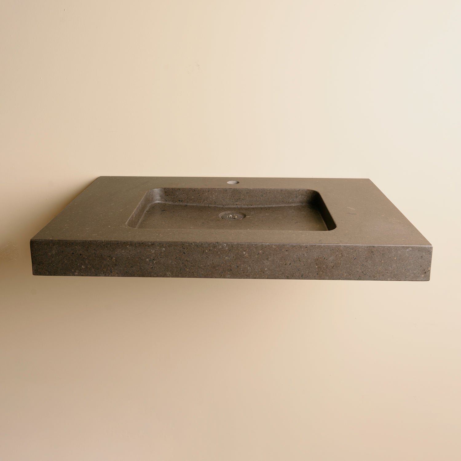 A contemporary bath vanity with an integral sink carved from a solid block of noce basalt. It has a center-hole faucet drilling.