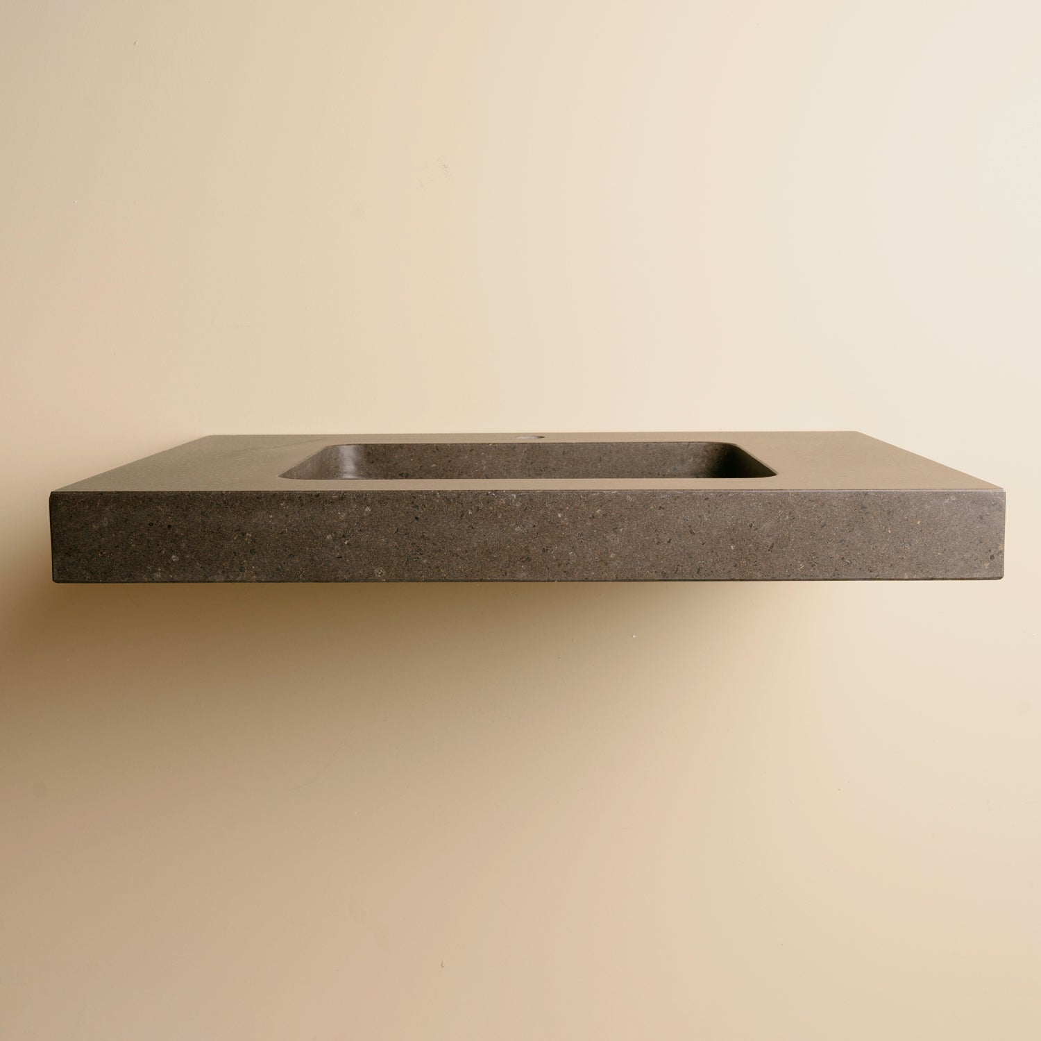 A contemporary bath vanity with an integral sink carved from a solid block of noce basalt. It has a center-hole faucet drilling.